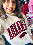 Load image into Gallery viewer, Person wearing a white Razorback sweatshirt with 'ARKANSAS' and a hog sweatshirt, standing in a Fayetteville ar store with razorback clothes, arkansas mockneck, razorback mockneck, arkansas razorback mock neck, arkansas mock neck, arkansas sweatshirt for women