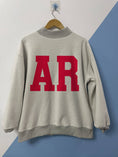Load image into Gallery viewer, Person wearing a white Razorback sweatshirt with 'ARKANSAS' and a hog sweatshirt, standing in a Fayetteville ar store with razorback clothes, arkansas mockneck, razorback mockneck, arkansas razorback mock neck, arkansas mock neck, arkansas sweatshirt for women