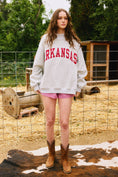 Load image into Gallery viewer, Woman wearing an 'ARKANSAS' sweatshirt in a rustic outdoor setting Arkansas reversible sweatshirt, razorback reversible sweater, Arkansas reversible shirt, Arkansas reversible shirt women’s, razorback store Fayetteville ar, Fayetteville boutiques, shopping near me, boutiques in the NWA mall