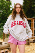 Load image into Gallery viewer, Woman wearing a gray sweatshirt with 'ARKANSAS' and red checkered shorts outdoors. Arkansas reversible sweatshirt, razorback reversible sweater, Arkansas reversible shirt, Arkansas reversible shirt women’s, razorback store Fayetteville ar, Fayetteville boutiques, shopping near me, boutiques in the NWA mall