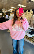 Load image into Gallery viewer, Woman wearing a pink sweatshirt with 'ARKANSAS' text, taking a mirror selfie in a clothing boutique Fayetteville ar, arkansas sweatshirt, pink arkansas sweatshirt, ribbed arkansas sweatshirt, pink ribbed arkansas sweatshirt