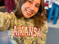 Load image into Gallery viewer, Woman wearing a camouflage Arkansas sweatshirt in Whimsy Whoo Boutique in their Arkansas Razorback Store. Camo Arkansas sweatshirt for women, camo Arkansas shirt, camo arkansas razorback shirt, camo arkansas razorback sweatshirt, camo arkansas crewneck, arkansas razorback store, women Arkansas sweatshirts