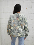 Load image into Gallery viewer, Woman wearing a camouflage Arkansas sweatshirt in Whimsy Whoo Boutique in their Arkansas Razorback Store. Camo Arkansas sweatshirt for women, camo Arkansas shirt, camo arkansas razorback shirt, camo arkansas razorback sweatshirt, camo arkansas crewneck, arkansas razorback store, women Arkansas sweatshirts