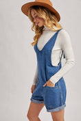 Load image into Gallery viewer, Woman wearing a denim overall romper and brown hat on a plain background, denim romper shorts, denim romper near me, Arkansas boutiques, clothing stores near me