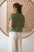 Load image into Gallery viewer, Woman wearing a green knitted top and white pants standing in front of a wooden wall art piece. Green sweater, green short sleeved sweater, green short sleeve sweater, blu pepper sweater, blu pepper green top, green top, shopping near me, boutiques Fayetteville ar