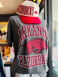 Load image into Gallery viewer, Gray t-shirt with 'Arkansas Razorbacks' logo and a matching cap worn by a person. grey Arkansas razorback tee, Arkansas razorback shirts, arkansas razorback boutique clothing, arkansas razorback shirts, razorback store, razorback apparel Fayetteville ar, arkansas razorback store