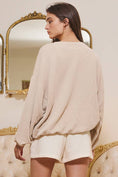 Load image into Gallery viewer, Woman wearing a beige sweater and white shorts standing in front of a decorative mirror.