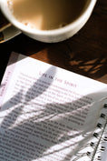 Load image into Gallery viewer, Open book with text on a wooden surface next to a cup of coffee