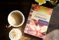 Load image into Gallery viewer, Bible study book titled 'Romans' by The Bible Study Collective next to a cup of coffee on a wooden surface.