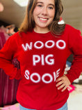 Load image into Gallery viewer, A woman in the vibrant red Wooo Pig Sooie Razorback sweatshirt, showcasing the high-quality chenille lettering for Arkansas gameday fans at Whimsy Whoo boutique store in FAyetteville, AR.