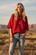 Load image into Gallery viewer, A model wearing The Gameday Essential Red Knit Oversized Sweater, a vibrant solid red short-sleeve knit top styled with distressed denim and turquoise jewelry for a trendy Arkansas gameday look.