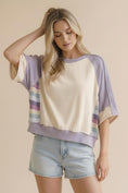 Load image into Gallery viewer, A full front view of the Lavender Lane Oversized Top from Whimsy Boutique in Fayetteville. This mixed-media top features a cream French Terry body, lavender waffle knit sleeves, and colorful striped side panels.