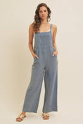 Load image into Gallery viewer, Woman wearing lenin-blend blue overalls against a plain background