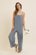 Load image into Gallery viewer, Woman wearing linen-blend blue overalls holding flowers against a plain background