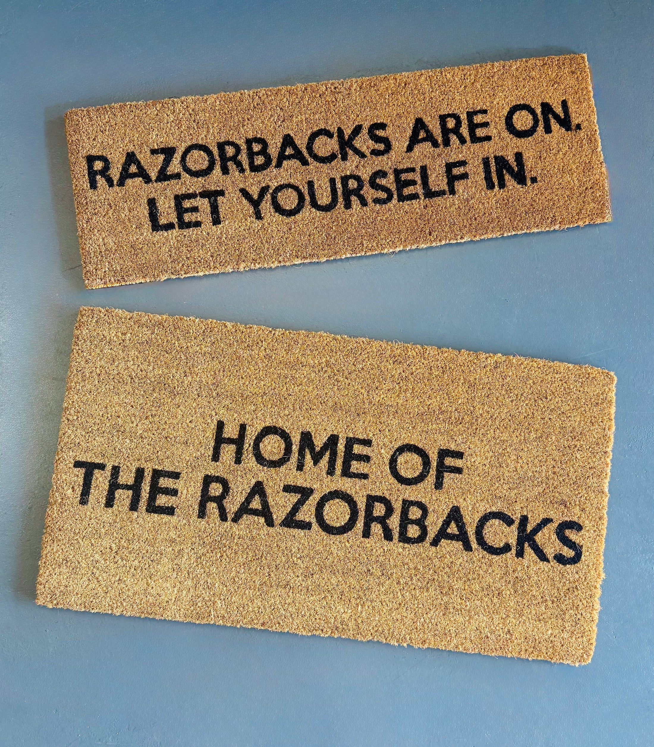 Two doormats with Razorbacks are on let yourself in text in a razorback store in Fayetteville, arkansas, razorback door mat, arkansas door mat, razorback welcome mat, Arkansas razorback door mat, razorback front door mat