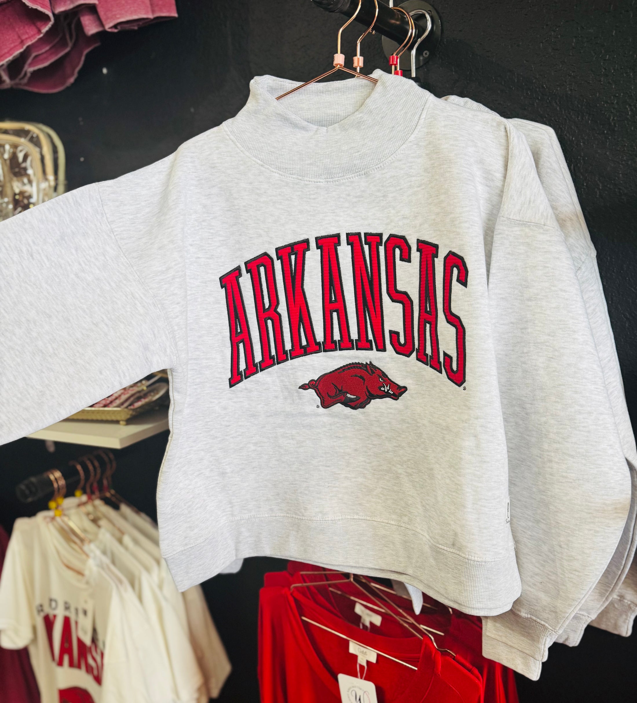 Gray sweatshirt with 'ARKANSAS' text and razorback on a rack in a Fayetteville ar stores, Arkansas mock neck sweatshirt, Arkansas mock neck, arknasas razorback women’s clothing, arknasas razorback boutique clothing, university of Arkansas clothing, H&M