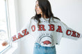 Load image into Gallery viewer, A woman wearing a white cropped long-sleeve top with 'RAZORBACK' text and the University of Arkansas at Fayetteville logo in red and black. Arkansas razorback store, cropped arkansas razorback long sleeve top, 
