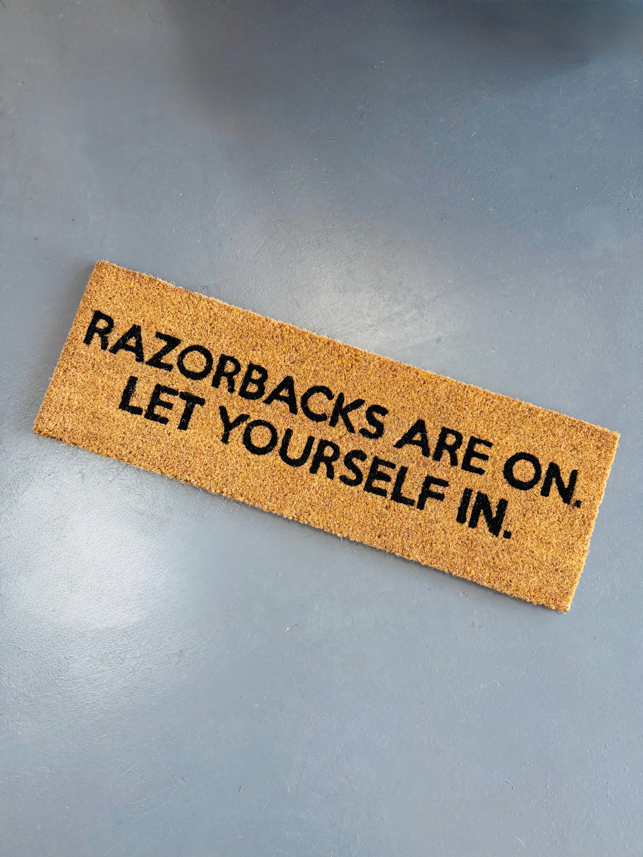 Doormat with 'Razorbacks are on. Let yourself in.' text in a store in Fayetteville, ar Two doormats with Razorbacks are on let yourself in text in a razorback store in Fayetteville, arkansas, razorback door mat, arkansas door mat, razorback welcome mat, Arkansas razorback door mat, razorback front door mat