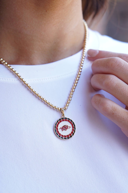 Necklace with a circular pendant featuring a red and black design on a white shirt. Razorback jewelry, razorback jewelry near me, razorback jewelry and accessories, Arkansas razorback jewelry, razorback charms for jewelry, razorback jewelry for sale, women razorback jewelry, Arkansas razorback pendant
