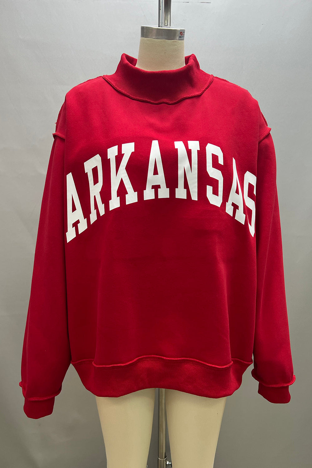 Red sweatshirt with 'ARKANSAS ' printed on it displayed on a mannequin against a gray background. red Arkansas reversible sweatshirt, red Arkansas reversible mock neck, Arkansas reversible sweatshirt, Arkansas reversible mock neck, AR reversible sweatshirt, AR reversible mock neck,  red AR reversible sweatshirt, red AR reversible mock neck, store near me, ARkansas reversible mock neck near me, Arkansas reversible sweatshirt near me