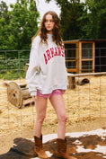 Load image into Gallery viewer, Person wearing a 'ARKANSAS' sweatshirt in an outdoor setting with trees and a wooden structure. Arkansas reversible sweatshirt, razorback reversible sweater, Arkansas reversible shirt, Arkansas reversible shirt women’s, razorback store Fayetteville ar, Fayetteville boutiques, shopping near me, boutiques in the NWA mall
