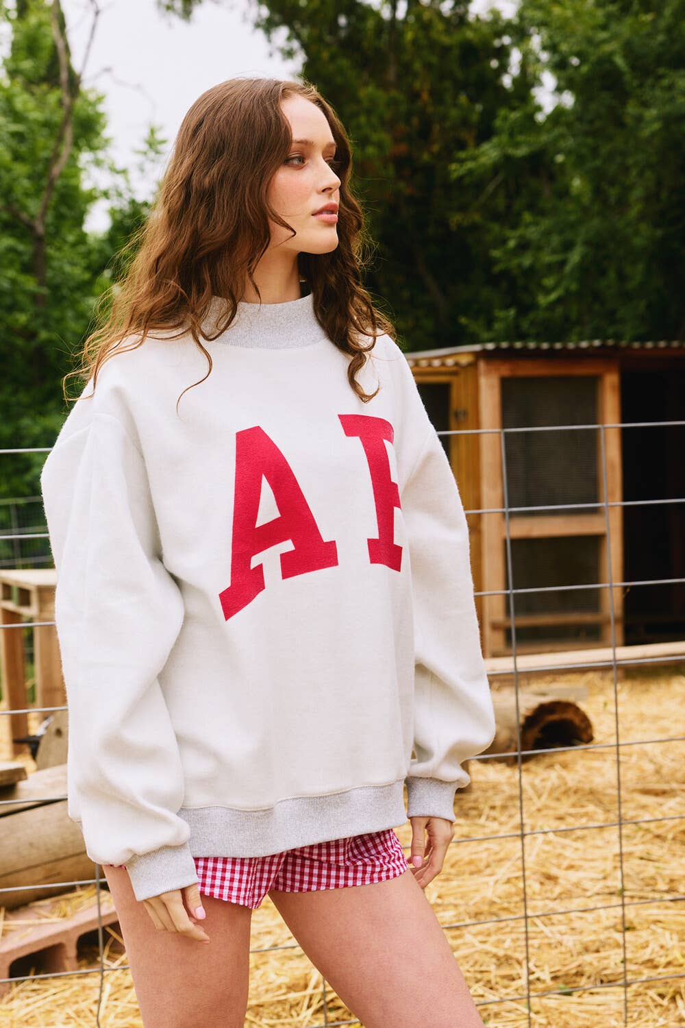 Woman wearing a white sweatshirt with red letters and pink shorts standing outdoors. Arkansas reversible sweatshirt, razorback reversible sweater, Arkansas reversible shirt, Arkansas reversible shirt women’s, razorback store Fayetteville ar, Fayetteville boutiques, shopping near me, boutiques in the NWA mall