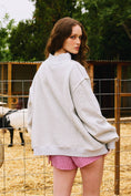 Load image into Gallery viewer, Woman wearing a gray sweatshirt and pink checkered shorts standing in front of a fence with a horse in the background. Arkansas reversible sweatshirt, razorback reversible sweater, Arkansas reversible shirt, Arkansas reversible shirt women’s, razorback store Fayetteville ar, Fayetteville boutiques, shopping near me, boutiques in the NWA mall
