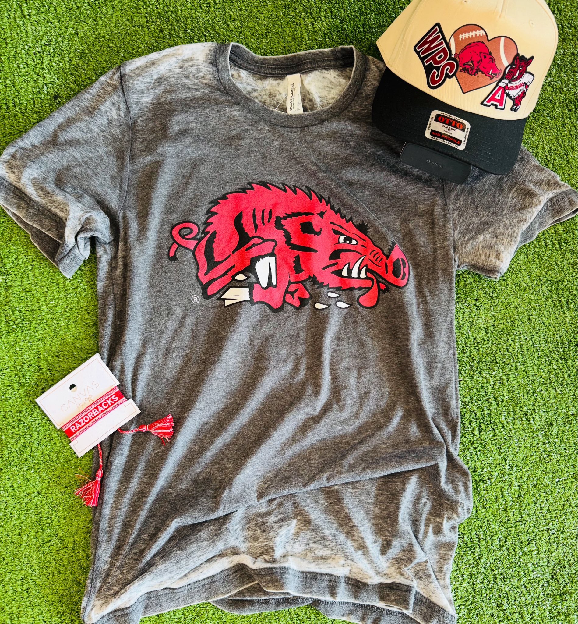 Gray t-shirt with red Razorback logo on a green surface, accompanied by a cap and tag, slobbering hog tshirt, whimsy whoo boutique razorback store, razorback t-shirts in Arkansas, razorbacks team shop