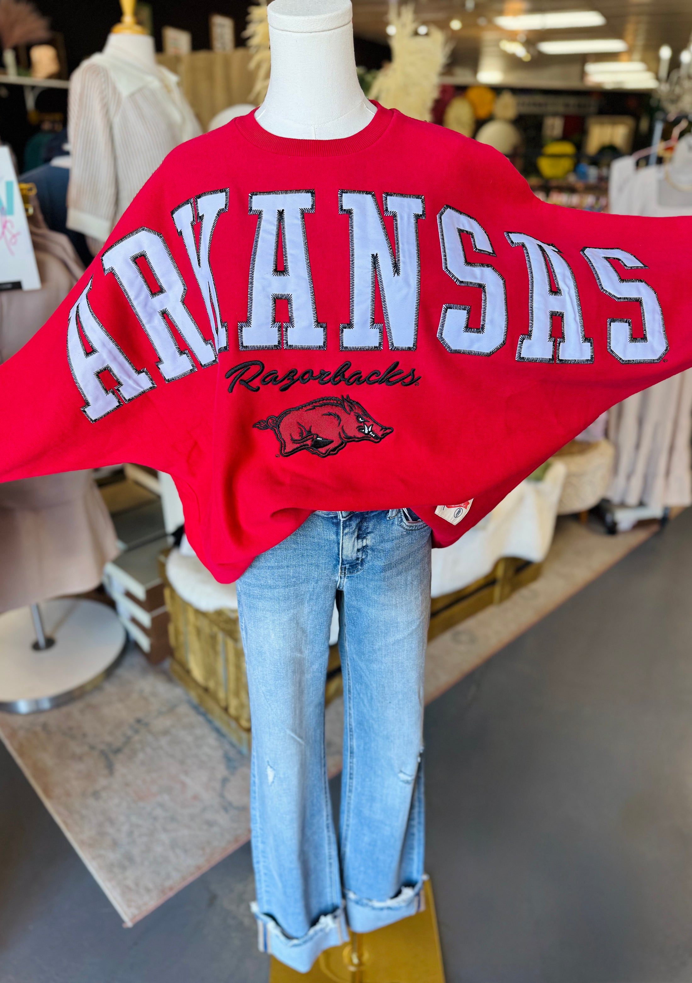 Red 'ARKANSAS Razorbacks' sweatshirt on a mannequin with jeans in a Fayetteville ar razorback store, boutique razorback clothing near me, arknasas sweatshirt for women, red Arkansas sweatshirt nearby