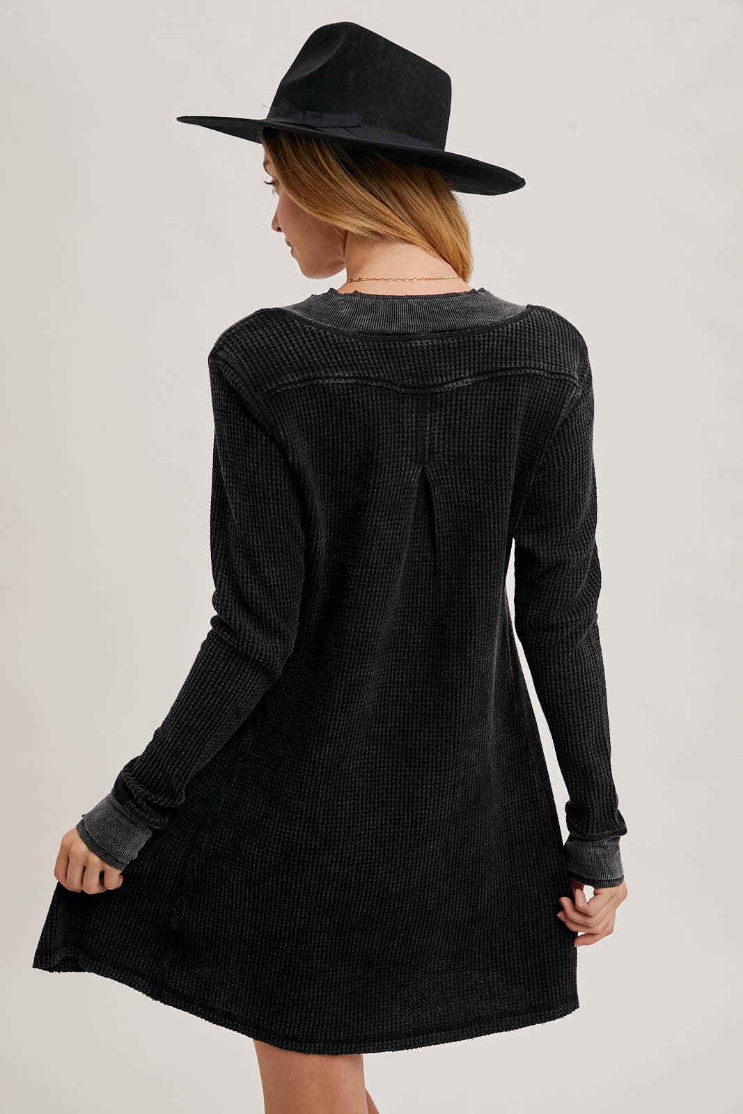 Person wearing a black dress and hat from behind on a light gray background, thermal knit dresses, waffle knit dress with sleeves, boutiques Fayetteville ar, clothing stores near me