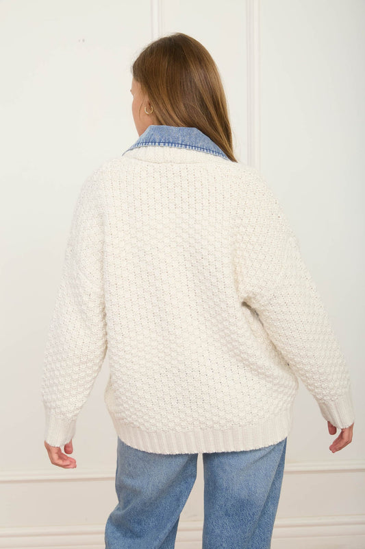 Woman wearing a white textured sweater and blue jeans in a Fayetteville Arkansas boutique store. Full-length view of the button-down long sleeve mixed media cable knit jacket with denim trim, a trending national outerwear style for women.