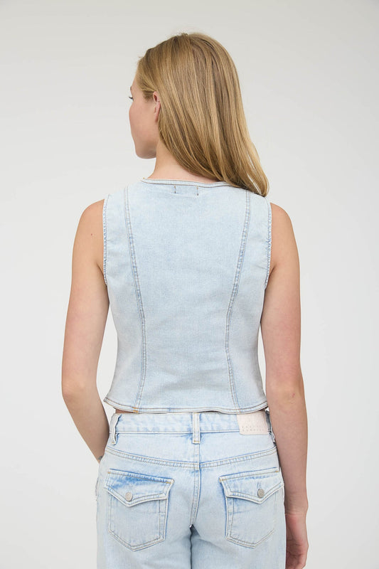 Person wearing a light blue denim vest and jeans on a plain background, light blue denim vest, light blue denim top, denim vest for women, fitted denim top, fitted denim vest, designer boutiques near me, boutiques Fayetteville, ar