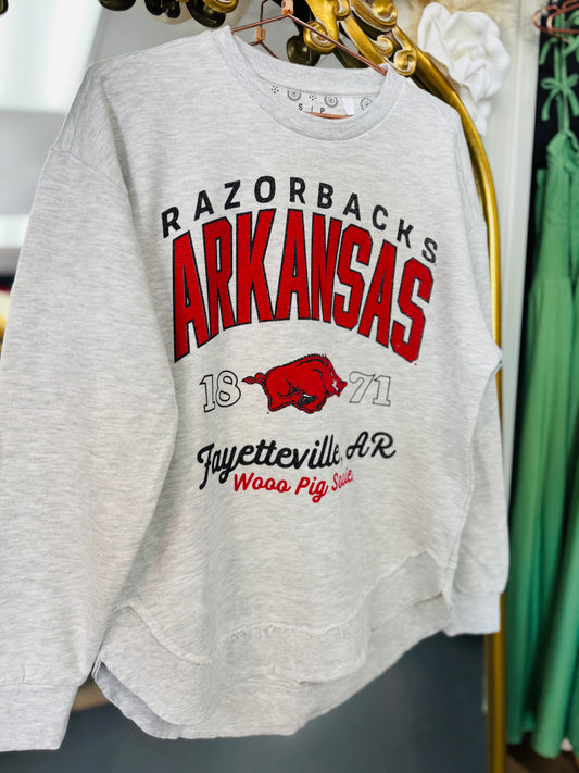 Gray sweatshirt with 'Razorbacks Arkansas' text and logo on a hanger. gray Razorback sweatshirt, Pressbox Arkansas sweatshirt, gray Arkansas sweatshirt, razorback shirts, Arkansas shirts, AR Razorback apparel, Razorback stores Fayetteville ar shopping