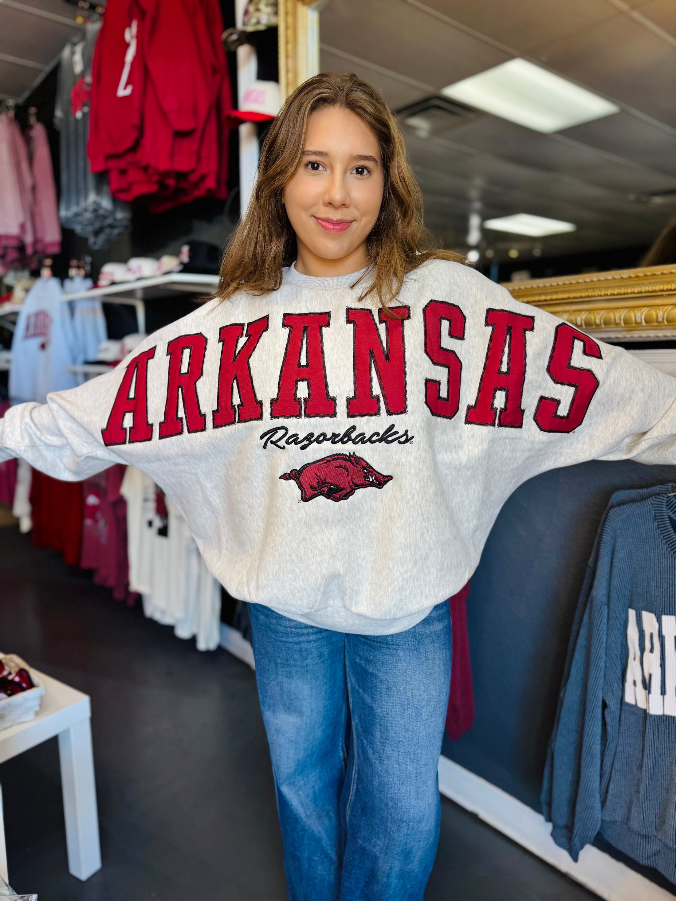 Woman wearing an Arkansas Razorbacks sweatshirt in a  Fayetteville ar razorback store, arkansas sweatshirts, Arkansas razorback shirt, razorback sweatshirts for women, arkansas razorback sweatshirt nearby, arkansas razorback store, store near me, Fayetteville ar stores, arkansas razorback store
