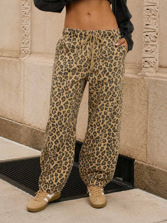 A woman wearing loose leopard-print drawstring pants, paired with beige sneakers and a dark cropped top, from Whimsy Whoo boutique in Fayetteville, AR