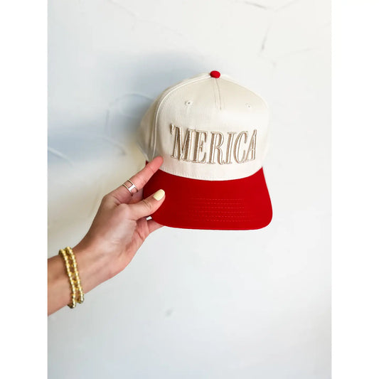 Hand holding a cap with 'MERICA' text against a light background, clothing stores