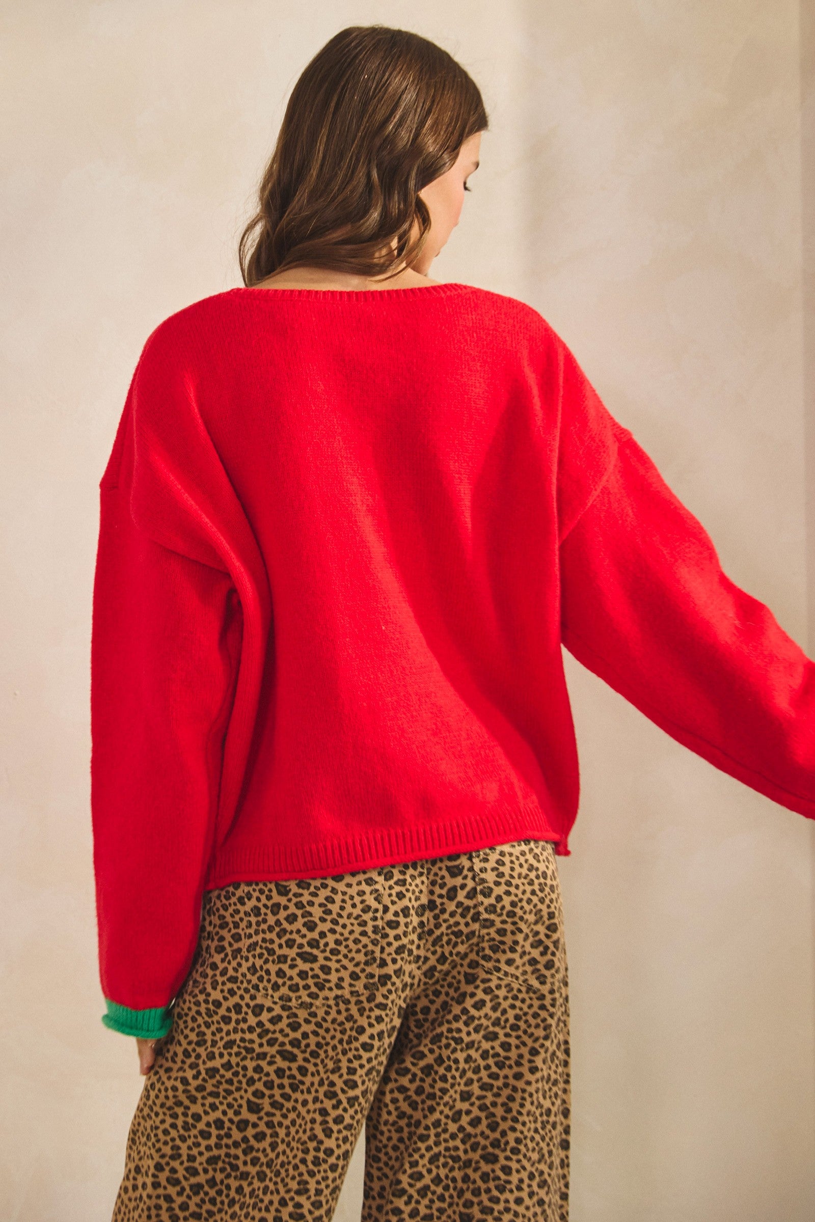 Woman wearing a red sweater and leopard print pants against a beige background, women’s christmas sweater, christmas sweater women, classy christmas sweater