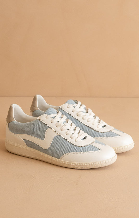 A pair of low top fashion sneakers with a denim upper and white vegan leather accents, featuring a lace-up closure and a rubber sole.