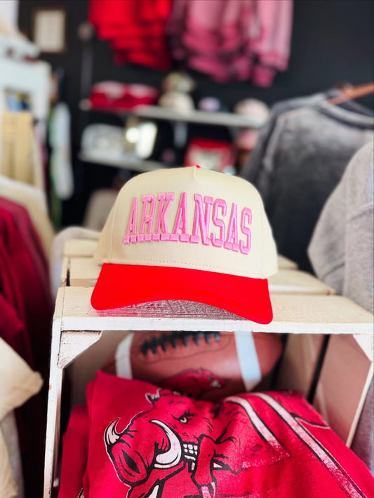 Beige and red cap with 'ARKANSAS' text on a shelf in a Fayetteville, AR Razorback Store. Pink Arkansas hats, pink razorback hats, razorback hats for women, razorback hats near me, Arkansas razorback boutique clothing