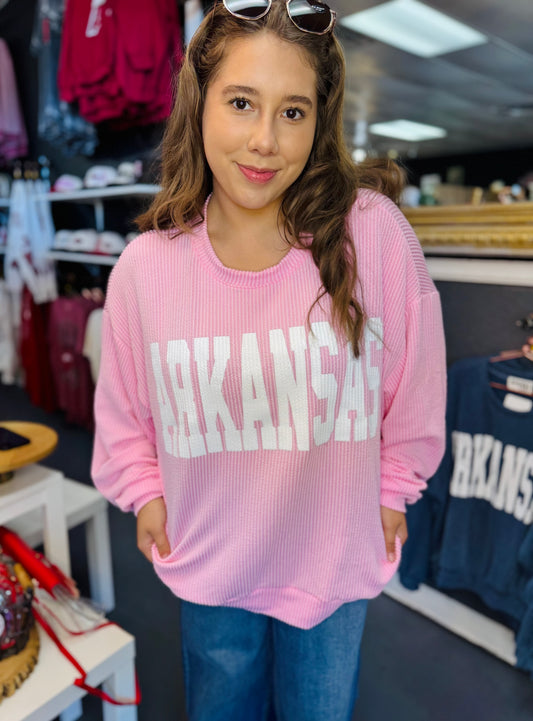 Woman wearing a pink 'ARKANSAS' ribbed sweatshirt in a clothing store Fayetteville ar. Pink ribbed arkansas sweatshirt, clothing stores Fayetteville ar