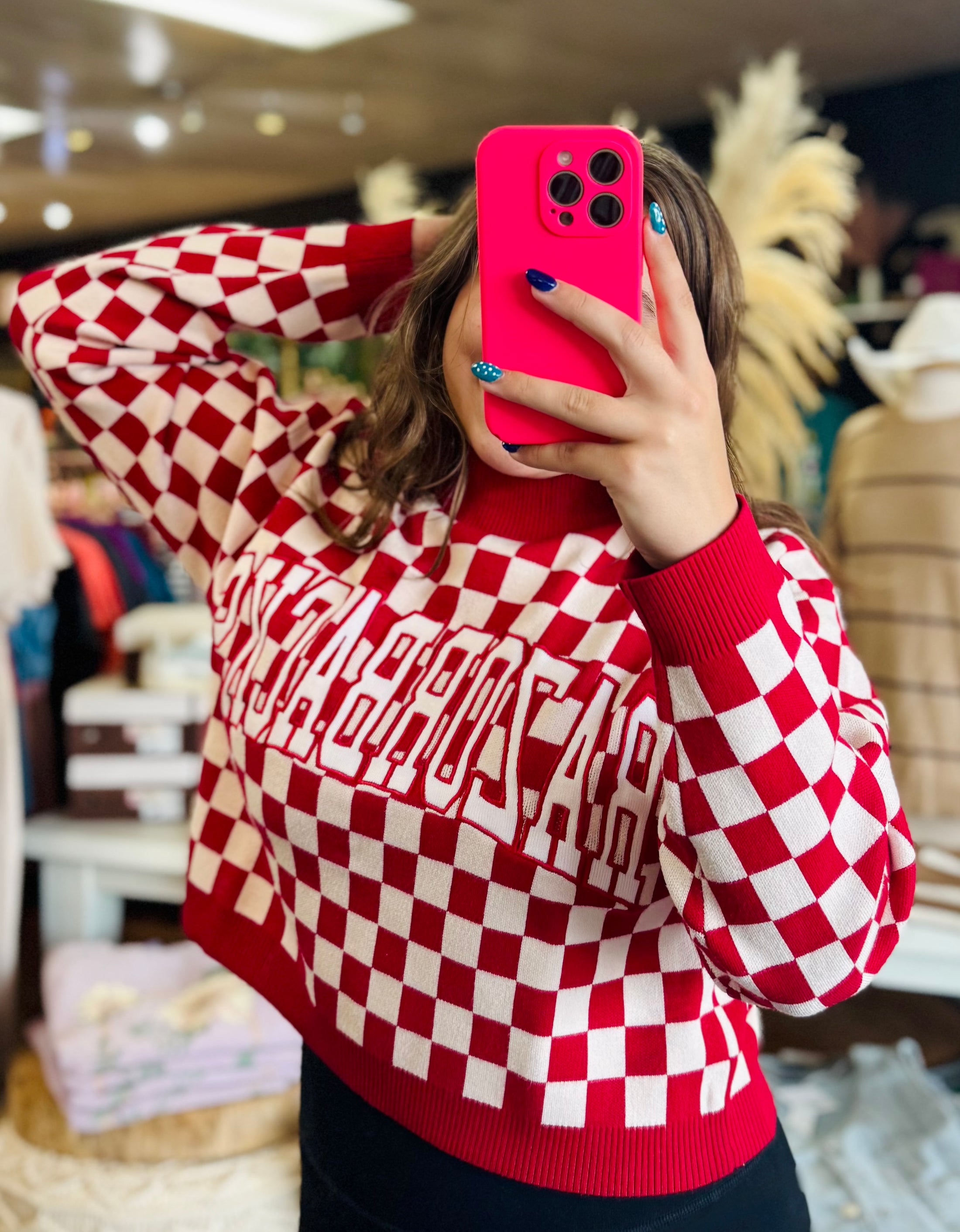 Woman wearing a red and white Razorback checkered sweater , taking a mirror selfie in an arkansas razorback store