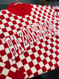 Load image into Gallery viewer, Red and white checkered sweater with 'ARKANSAS' text on a dark background in a Fayetteville arkansas razorback store
