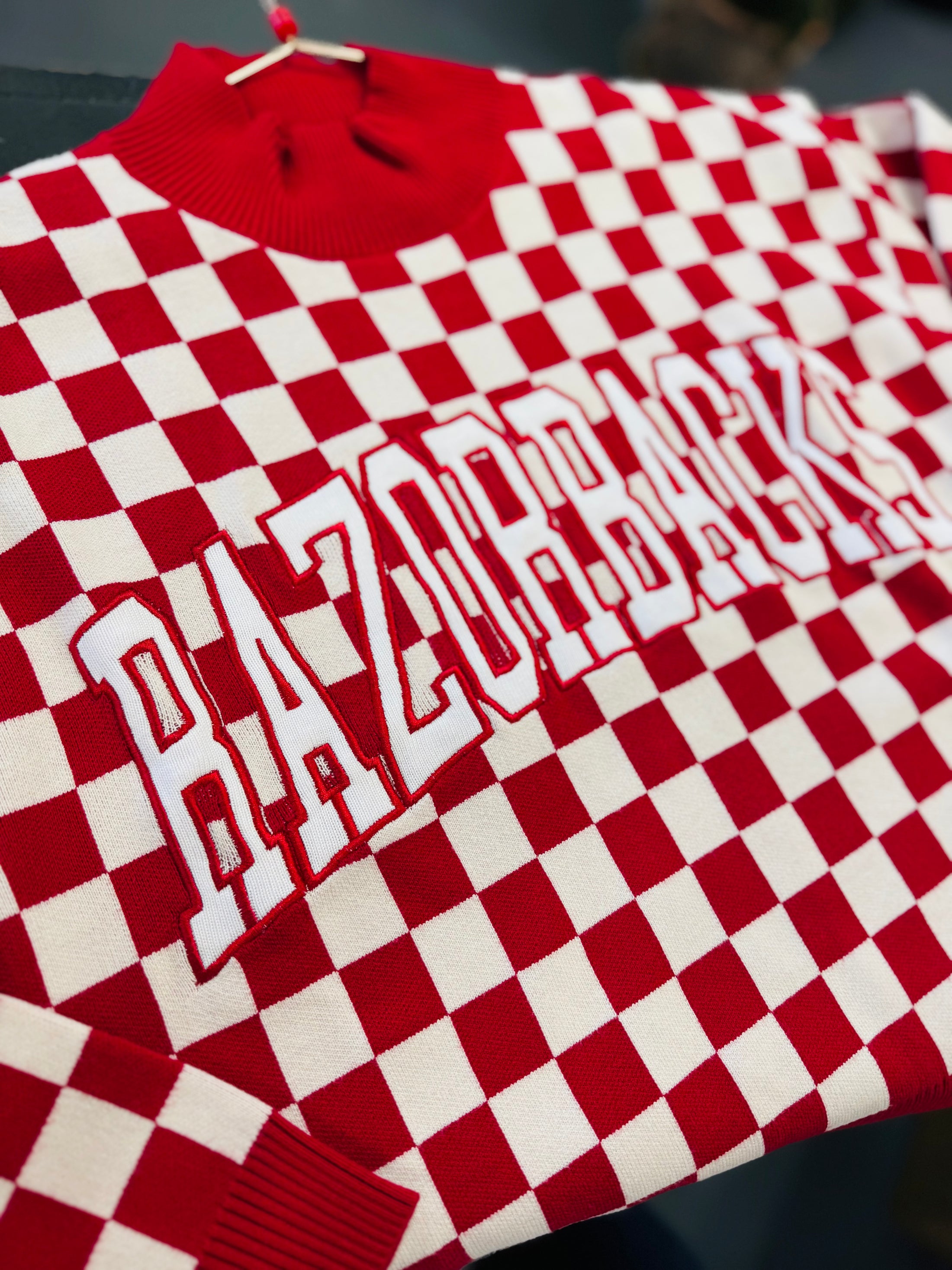 Red and white checkered sweater with 'ARKANSAS' text on a dark background in a Fayetteville arkansas razorback store