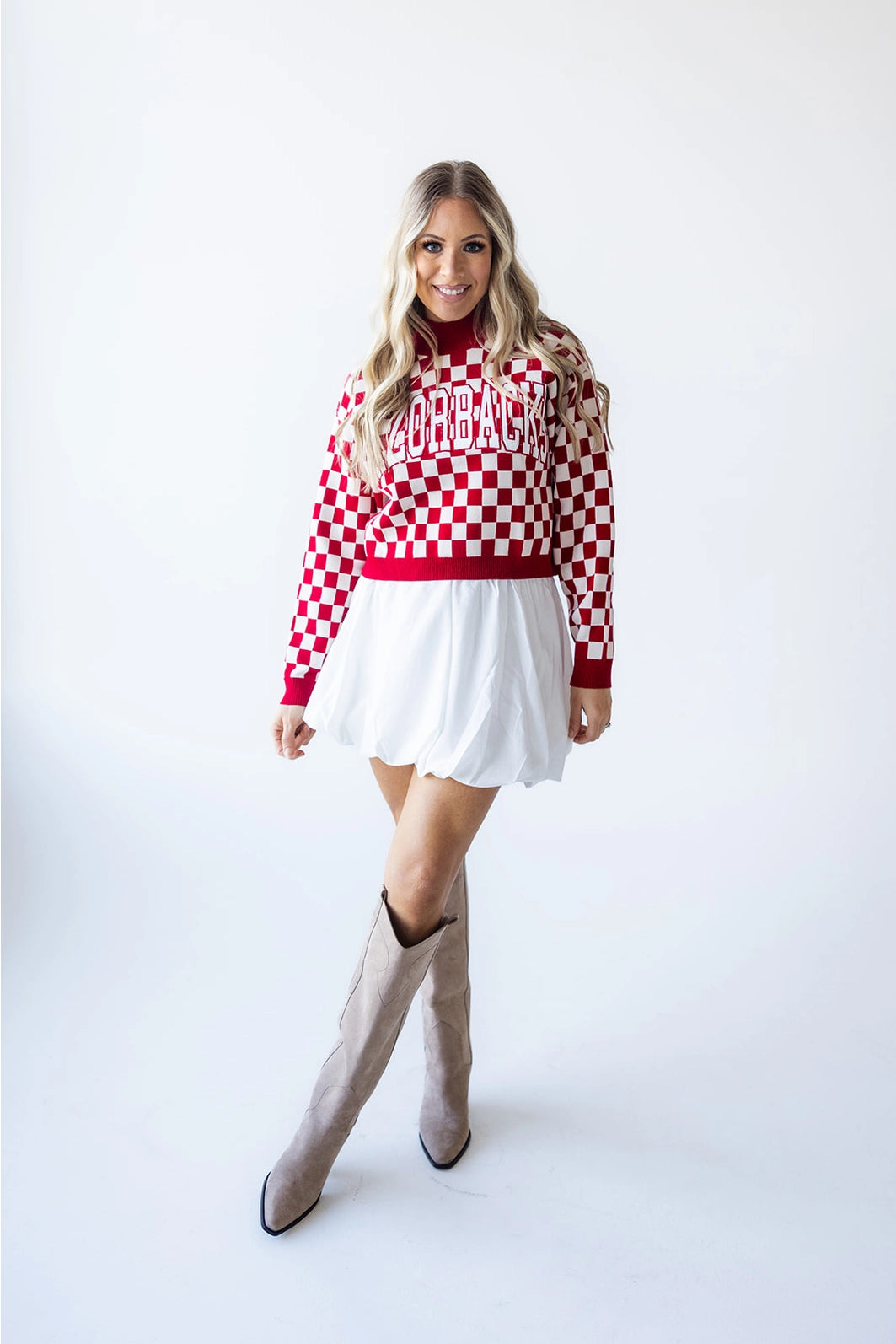 Woman wearing a red and white checkered sweater with 'Arkansas' text, white skirt, and knee-high boots on a white background in a Fayetteville arkansas store