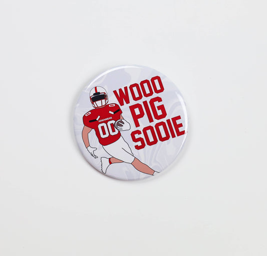Button badge with football player graphic and 'Wood Pig Sooie' text on a white background, arkansas razorback jewelry and accessories, boutiques open now, razorback store Fayetteville ar