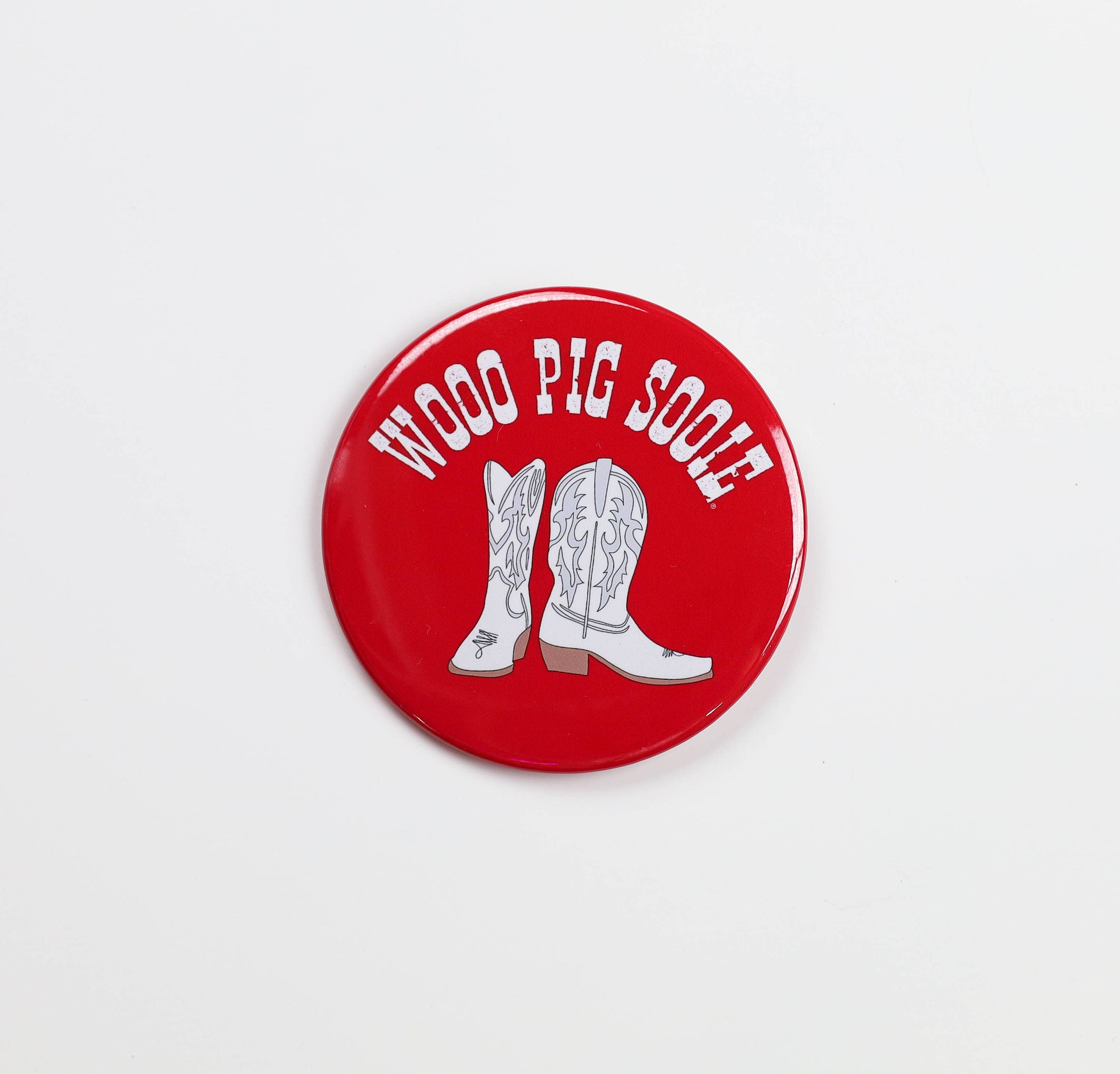 Red button with white cowboy boots and 'Woof Pig Sooie' text on a light gray background, gameday buttons near me, razorback stores in Fayetteville arkansas, clothe boutique