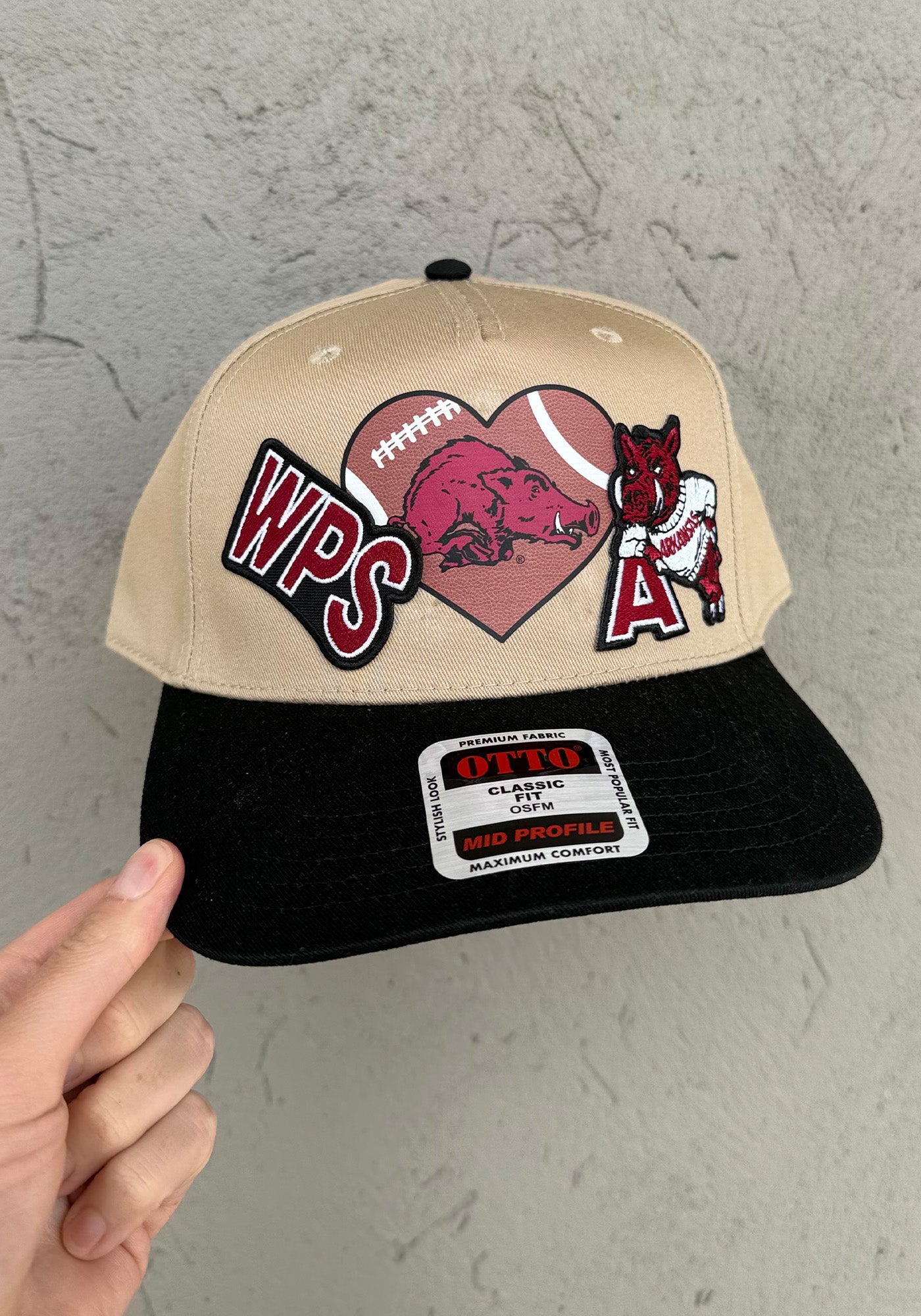 Beige and black Arkansas razorbackcap with razorback football patches designs and text on a gray background. Razorback hats near me, razorback trucker hat, women razorback trucker hat, razorback boutique clothing