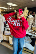 Load image into Gallery viewer, Woman wearing a red 'Arkansas' sweatshirt taking a mirror selfie in a Fayetteville razorback store. Arkansas Razorback sweatshirt near me, razorback store online
