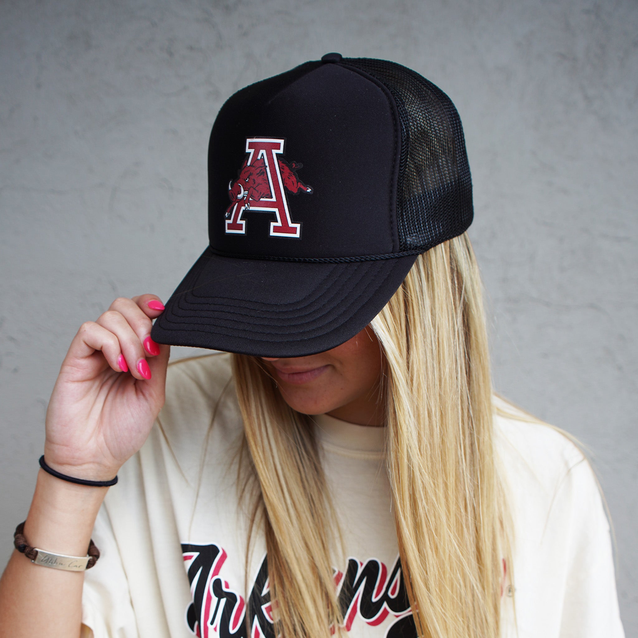 A person wearing a black baseball hat with a red Arkansas Razorback logo in the shape of a letter 'A'. Razorback black hat, razorback hat, razorback baseball hat, razorback trucker, razorback trucker hat