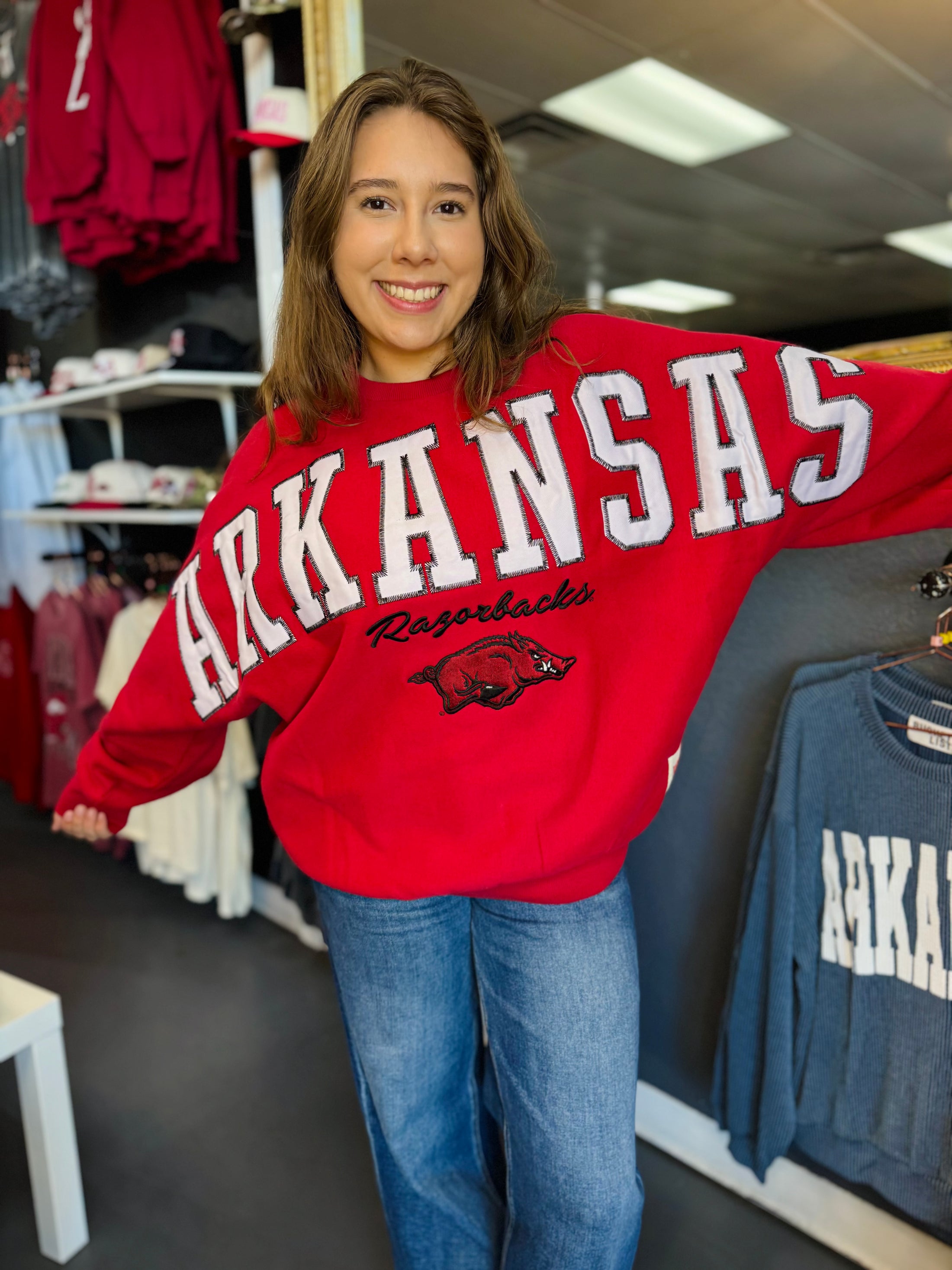 woman in Fayetteville ar razorback store wearing a red oversized razorback sweatshirt with oversize arkansas letters and a hog logo, arkansas sweatshirts, razorback shirt, razorback store near me